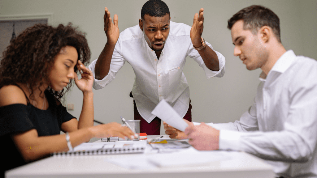 A woman and a man in a heated discussion while a third man, seemingly frustrated, tries to intervene—representing workplace conflict or stress.