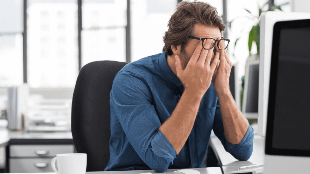 A stressed man sitting at a desk with his head in his hands, possibly overwhelmed by work or facing burnout.