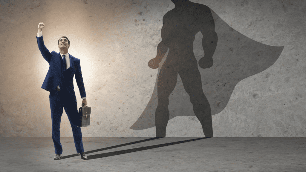 A man in formal attire standing confidently in front of a wall where his shadow appears as a superhero in a cape.